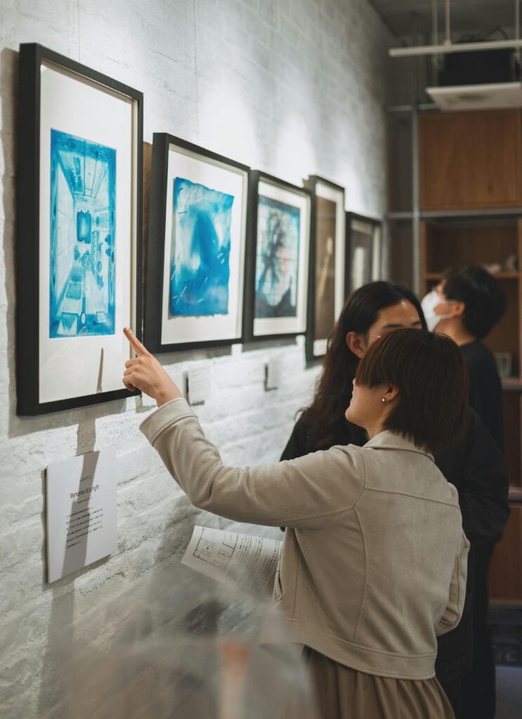 Visitors discuss artworks at a modern gallery in Shinjuku, showcasing blue-toned prints.
