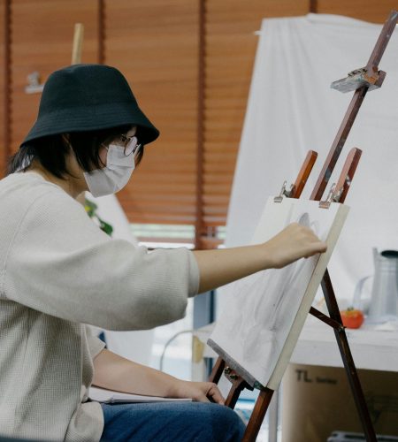 Giới Thiệu An artist wearing a mask sketches on a canvas in a Shinjuku art studio, Tokyo, Japan.